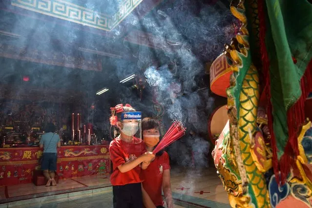 A girl wearing a protective mask and face shield holds incense sticks while praying with her mother at the Surya Dharma temple during the Lunar New Year celebrations in Pekanbaru, Riau province, Indonesia, February 12, 2021. (Photo by FB Anggoro/Antara Foto via Reuters)