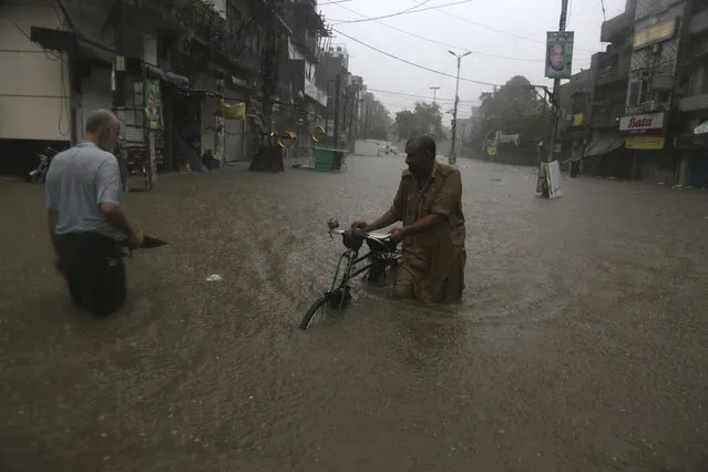 People wade through a flooded road after heavy rain fall in Lahore, Pakistan, Tuesday, July 3, 2018. Heavy rain lashed Lahore causing several rain-linked accidents. (Photo by K.M. Chaudary/AP Photo)