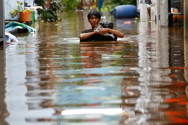 A man carrying his goods walks through the water in an area affected by floods, following heavy rains in Jakarta, Indonesia, February 20, 2021. (Photo by Ajeng Dinar Ulfiana/Reuters)
