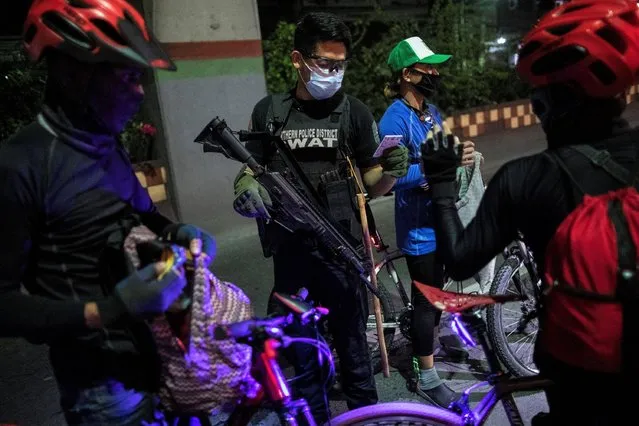 An armed police officer checks the IDs of cyclists at a checkpoint placed to implement a curfew in the country's capital amid rising coronavirus disease (COVID-19) cases, in Caloocan City, Metro Manila, Philippines, March 16, 2021. (Photo by Eloisa Lopez/Reuters)