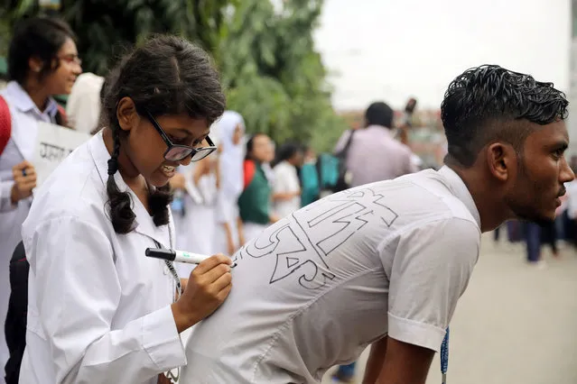 A student writes a slogan on the back of another student as they take part in a protest over recent traffic accidents that killed a boy and a girl, in Dhaka, Bangladesh on August 4, 2018. (Photo by Mohammad Ponir Hossain/Reuters)