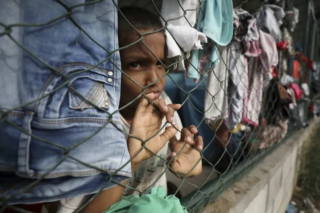 A child looks through a fence at a shelter set up in a community center in Arauquita, Colombia, Thursday, March 25, 2021, on the border with Venezuela. Venezuelans are seeking shelter in Colombia this week following clashes between Venezuela's military and a Colombian armed group along the shared border. (Photo by Fernando Vergara/AP Photo)