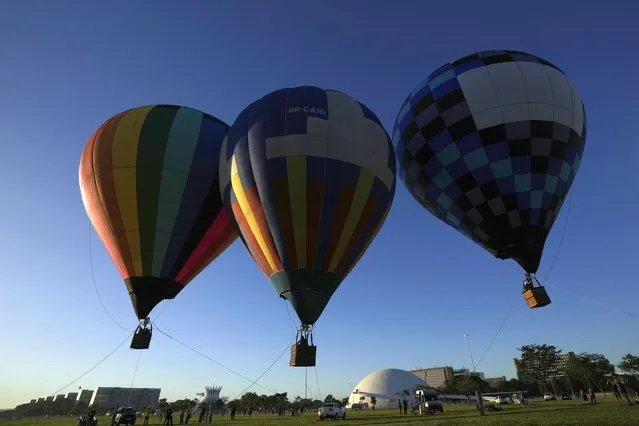 Hot air balloons are suspended at the Esplanade of Ministries complex during a cultural festival in Brasilia, Brazil, at sunrise Friday, March 31, 2023. (Photo by Eraldo Peres/AP Photo)