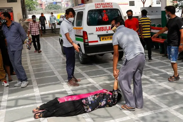 A man tries to lift a woman that fainted after seeing the body of a relative who died from the coronavirus disease (COVID-19), at a crematorium in New Delhi, India, April 30, 2021. (Photo by Adnan Abidi/Reuters)