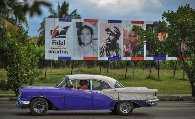 An old car drives past a billboard depicting Cuban revolutionary leader Fidel Castro and reading “Fidel Among Us”, in Havana, on November 27, 2016 two days after his death. Cuban revolutionary icon Fidel Castro died late November 25 in Havana, his brother, President Raul Castro, announced on national television. Castro's ashes will be buried in the historic southeastern city of Santiago on December 4 after a four-day procession through the country. (Photo by Yamil Lage/AFP Photo)