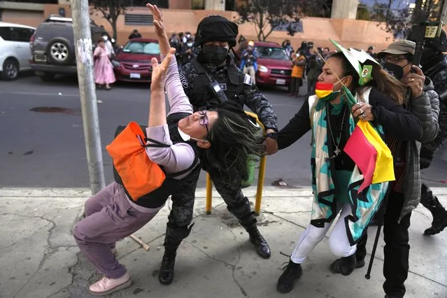 A police officer tries to prevent an anti-government protester from pulling the hair of a woman who is part of group that appeared to show their support for the government during a march of healthcare workers critical of the government, in La Paz, Bolivia, on July 21, 2022. (Photo by Juan Karita/AP Photo)