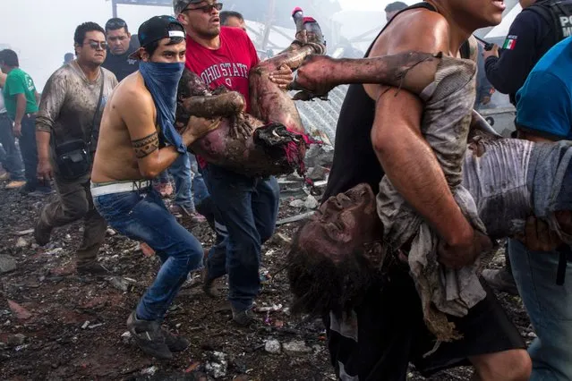 Victims severely burned are taken away by rescuers from the smoldering ruins of a fireworks market, flattened by a huge blast that killed at least 26 and injured dozens, in Mexico City, on December 20, 2016. The conflagration, in the suburb of Tultepec, set off a quickfire series of multicolored blasts and a vast amount of smoke that hung over Mexico City. (Photo by Israel Gutierrez/AFP Photo)