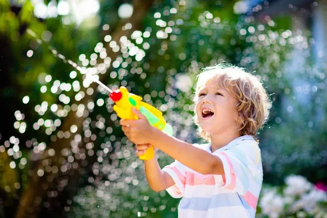 Kids play with water gun toy in garden. Outdoor summer fun. Little boy playing with water hose in sunny backyard. Party game for children. Healthy activity for hot sunny day. (Photo by FamVeld/Rex Features/Shutterstock)