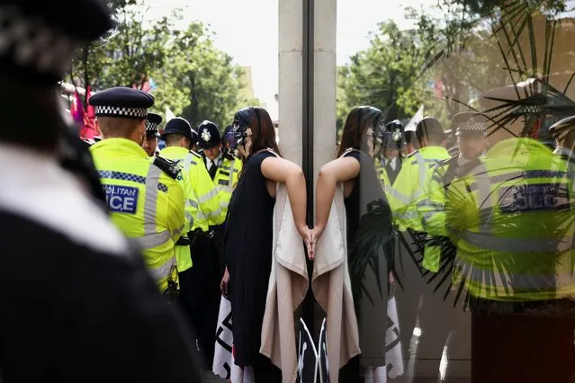Police officers stand next to an activist who glued herself to the window of the Selfridges department store during an Extinction Rebellion climate activists' protest, at Oxford Street, in London, Britain on August 24, 2021. (Photo by Henry Nicholls/Reuters)