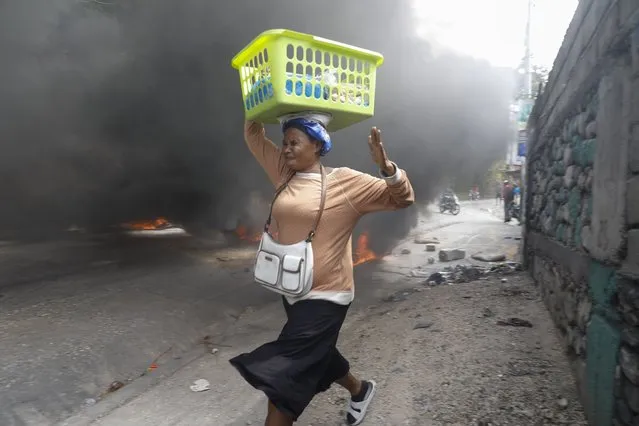A woman walks past burning tires during a protest against Haitian Prime Minister Ariel Henry in Port-au-Prince, Haiti, Monday, February 5, 2024. Protests have shut down major cities in Haiti as demonstrators clash with police and demand the resignation of Prime Minister Ariel Henry. (Photo by Odelyn Joseph/AP Photo)