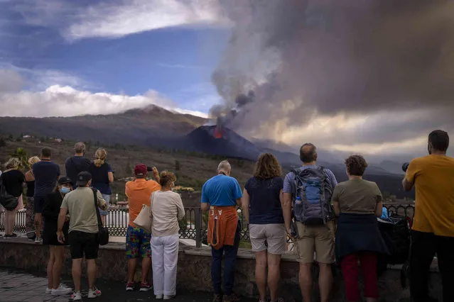 Tourists look and take photos at a volcano as it continues to erupt on the Canary island of La Palma, Spain, Tuesday, October 26, 2021. Officials say a volcano erupting for the past five weeks on the Spanish island of La Palma is more active than ever. New lava flows have emerged following a partial collapse of the crater and threaten to engulf previously unaffected areas. (Photo by Emilio Morenatti/AP Photo)