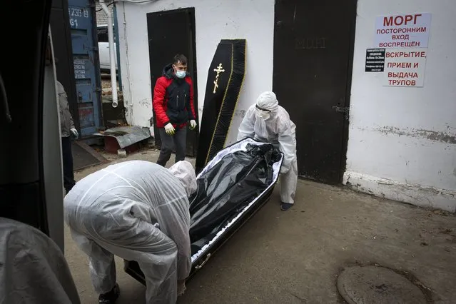 Medical workers in protective suits move a coffin with the body of a COVID-19 victim at the morgue of Infectious Hospital No. 5 in Nizhny Novgorod, Russia, on Wednesday, October 20, 2021. The low vaccination rate in Russia, where only about a third of the population is fully vaccinated, is causing concern as the country suffers a sharp rise in cases, setting records for infections and deaths nearly every day this month. ​(Photo by Roman Yarovitcyn/AP Photo)
