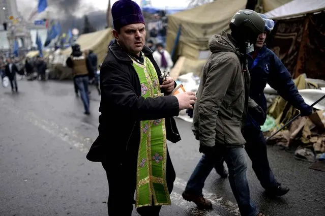 A priest rushes to give the last sacraments to an anti-government protester during clashes with riot police in central Kiev on February 20, 2014 in Kiev. (Photo by Bulent Kilic/AFP Photo)