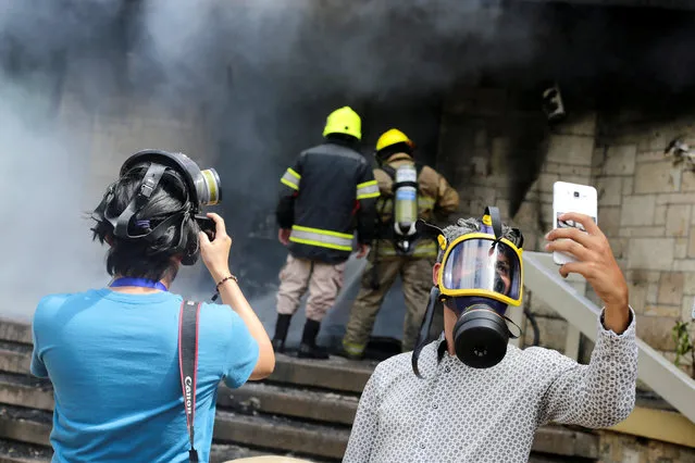 A journalist takes a selfie as firefighters extinguish burning tires, set alight at the entrance of the U.S. embassy by demonstrators during a protest against President Juan Orlando Hernandez government's plans to privatise healthcare and education, in Tegucigalpa, Honduras on May 31, 2019. (Photo by Jorge Cabrera/Reuters)