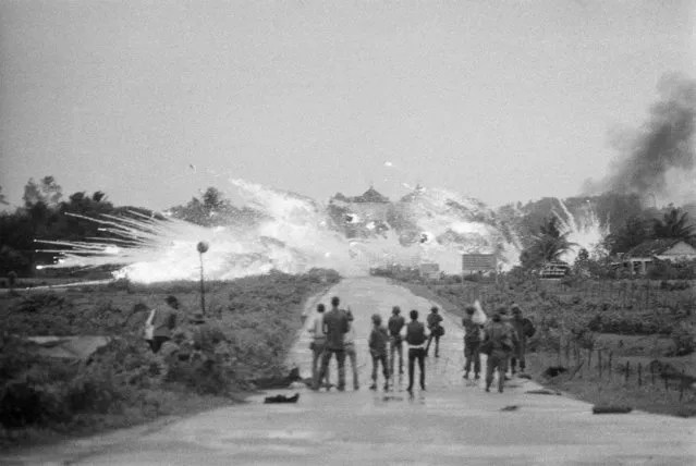 In this June 8, 1972 file photo, vombs with a mixture of napalm and white phosphorus jelly dropped by Vietnamese AF Skyraider bombers explode across Route-1, amidst homes and in front of the Cao Dai temple in the outskirts of Trang Bang, Vietnam. In the foreground are Vietnamese soldiers and journalists from various international news organizations. The towers of the Trang Bang Cao Dai temple are visible in the centre of the explosions. (Photo by Nick Ut/AP Photo)