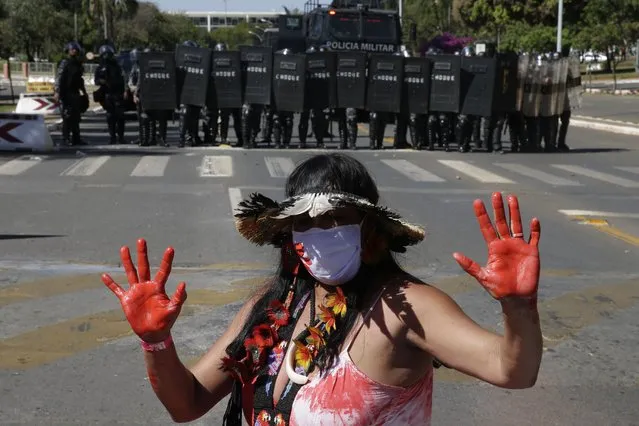 An Indigenous woman stands in front of a formation of riot police blocking a road, outside Congress in Brasilia, Brazil, Tuesday, June 22, 2021. Indigenous are camping in the capital to oppose a proposed bill they say would limit recognition of reservation lands. (Photo by Eraldo Peres/AP Photo)