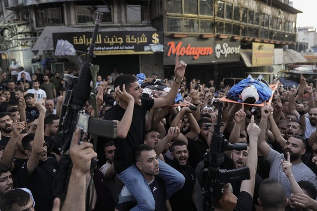 Gunmen hold up their weapons as mourners carry the bodies of Palestinians, one of them draped in the Islamic Jihad militant group flag, during their funeral in the West Bank city of Jenin, Thursday, June 6, 2024. (Photo by Majdi Mohammed/AP Photo)