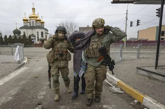 Ukrainian servicemen help an elderly woman, in the town of Irpin, Ukraine, Sunday, March 6, 2022. (Photo by Andriy Dubchak/AP Photo)