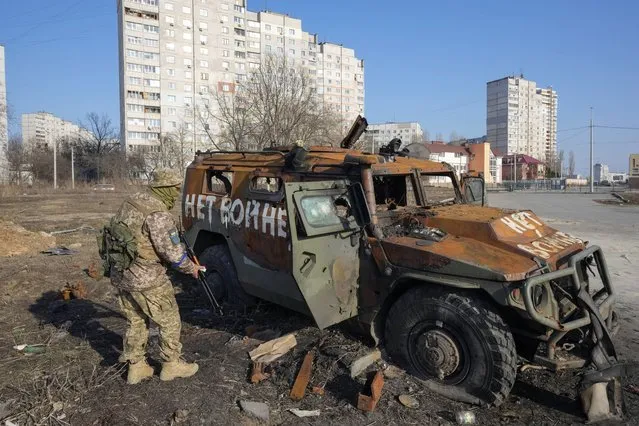 A Ukrainian soldier inspects a destroyed Russian APC after recent battle in Kharkiv, Ukraine, March 24, 2022. The writing made by Ukrainian soldiers reads: “Not to War”. (Photo by Efrem Lukatsky/AP Photo)