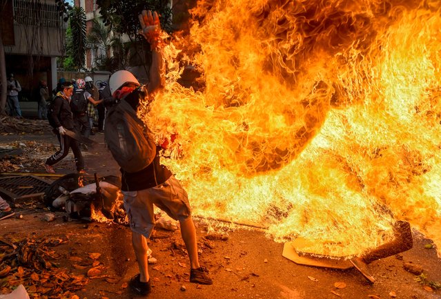 A man tries to help a fellow demonstrator who catched fire, after the gas tank of a police motorbike exploded, during clashes in a protest against Venezuelan President Nicolas Maduro, in Caracas on May 3, 2017. (Photo by Juan Barreto/AFP Photo)