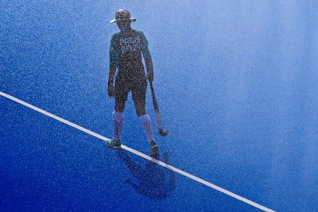 Water is sprayed on the pitch as a ball girl walks along the center line before the start of the men's Group A field hockey match between South Africa and Germany at the Yves-du-Manoir Stadium during the 2024 Summer Olympics, Tuesday, July 30, 2024, in Colombes, France. (Photo by Aijaz Rahi/AP Photo)