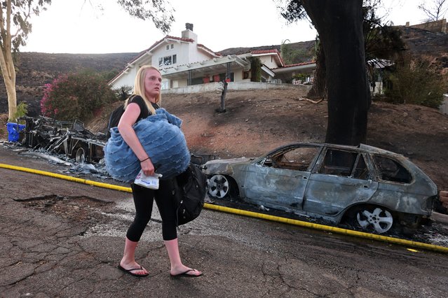 A resident leaves with their belongings as the Edgehill Fire destroyed several homes and vehicles during a hot day with temperatures reaching 107 Fahrenheit (41.6 Celsius) in San Bernardino, California, August 5, 2024. A wildfire burned a San Bernardino hillside community (60 miles / 96km east of Los Angeles) on the afternoon of August 5. Initial reports indicated that the fire had grown to at least 100 acres. By 6 p.m., county firefighters reported that the fire was down to 54 acres (22 hectares) and 25% contained. (Photo by David Swanson/AFP Photo)