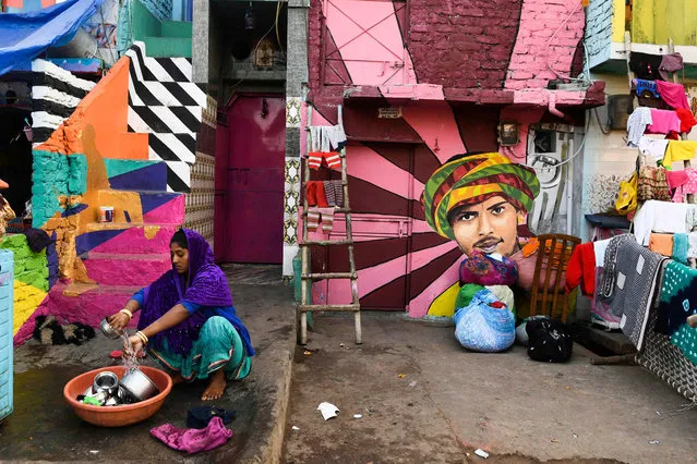 A woman washes utensils in front of her home adorned with murals painted by artists from “Delhi Street Art” group at the Raghubir Nagar slum in New Delhi on December 2, 2019. (Photo by Sajjad Hussain/AFP Photo)