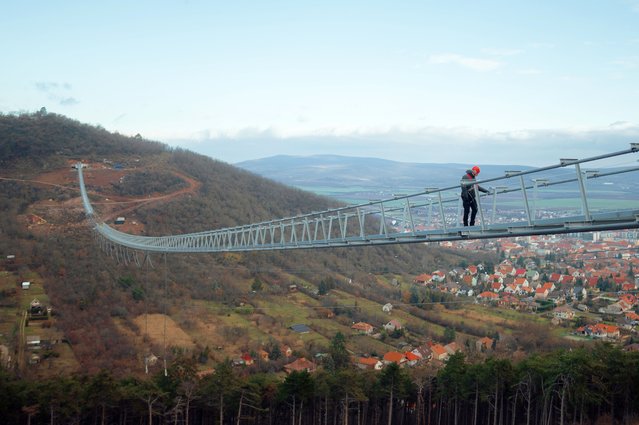 Attila Kecskes, head of the building site, carries out a general inspection of the building process of the world's longest two-way suspension bridge, which is expected to be officially opened to the public around April-May 2024, in Satoraljaujhely, Hungary on December 15, 2023. The nearly 800-meter-long structure connects the two points of the city, Var-Hill and Szar-Hill, at a height of 80 meters. The bridge, which will have a glass floor in the central part, is being built as part of the Tokaj-Zemplen Development Programme, with a budget of £9.3 million (HUF 4 billion). The walkway will have a width of 1.2m and descend by 27m at its lowest point, resulting in a 15% steepness at its most extreme. The design of bridge prioritizes minimal physical impact on the landscape, eliminating the need for large pylons. Additionally, the footpath has been crafted to seamlessly blend into the silhouettes of the surrounding mountains. The new pedestrian bridge will later become part of the Zemplen Adventure Park, a fully municipal project. (Photo by Robert Nemeti/Anadolu via Getty Images)