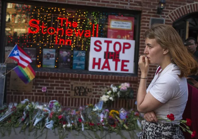 A woman cries and holds flowers in front of a makeshift memorial to remember  the victims of a mass shooting in Orlando, Fla., in New York, Sunday, June 12, 2016.  A gunman wielding an assault-type rifle and a handgun opened fire inside a crowded gay nightclub early Sunday before dying in a gunfight with SWAT officers. (Photo by Andres Kudacki/AP Photo)
