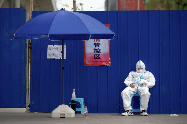 A security guard wearing personal protective equipment (PPE) sleeps next to an entrance of a residential area under lockdown due to Covid-19 coronavirus restrictions in Beijing on May 12, 2022. (Photo by Noel Celis/AFP Photo)