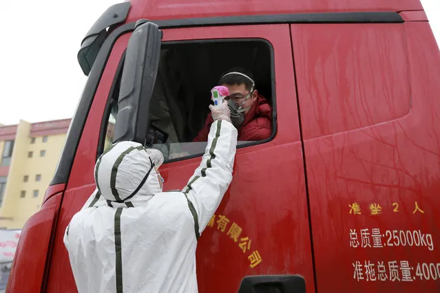 A worker in a hazardous materials suit takes the temperature of a truck driver at a checkpoint in Huaibei in central China's Anhui Province, Monday, January 27, 2020. China on Monday expanded sweeping efforts to contain a viral disease by extending the Lunar New Year holiday to keep the public at home and avoid spreading infection as the death toll rose to 80. (Photo by Chinatopix via AP Photo)