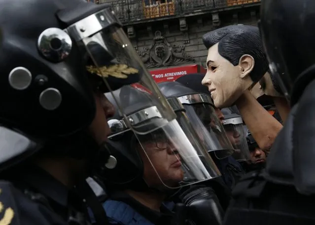 A member of the National Coordinator of Workers of Education of Mexico (CNTE) holds a mask resembling Mexican President Enrique Pena Nieto, surrounded by policemen, during a protest against the education reform, in Mexico City, Mexico, 05 July 2016. The CNTE, a union with its biggest support in the poorest states, Oaxaca, Michoacan, Guerrero, is battling for the abolition of an education reform enacted by Mexican Government in 2013. (Photo by Jorge Nunez/EPA)