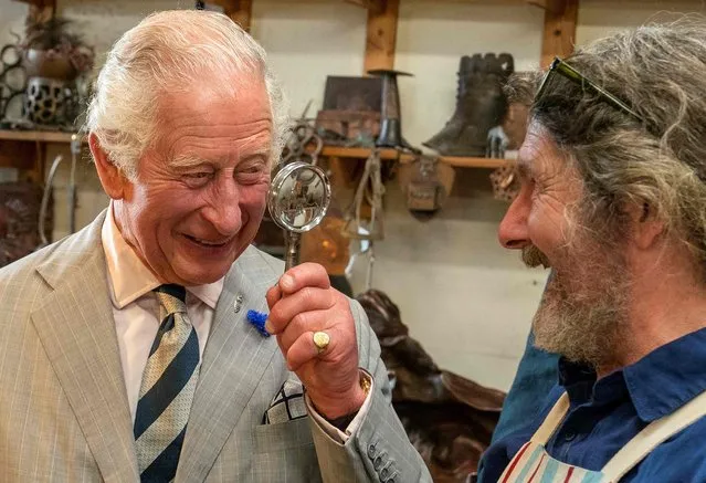 Britain's Prince Charles, Prince of Wales (L), holds a magnifying glass as he jokes with Michael Johnson during a visit to The Copper Works, a workshop specialising in the use of copper, during his visit to Newlyn near Penzance in southwest England, on July 18, 2022. Their Royal Highnesses met local fisherman and learnt about the sustainable fishing practices that they are adopting. (Photo by Arthur Edwards/Pool via AFP Photo)