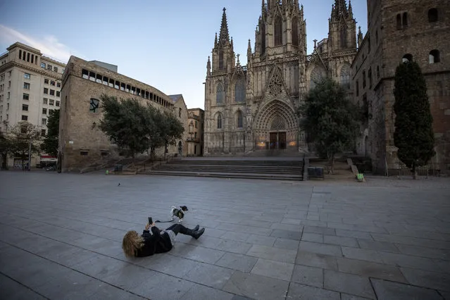A woman takes a photo of her dog in front of the Barcelona's cathedral, Spain, Sunday, March 15, 2020. Spain's government announced Saturday that it is placing tight restrictions on movements and closing restaurants and other establishments in the nation of 46 million people as part of a two-week state of emergency to fight the sharp rise in coronavirus infections. For most people, the new coronavirus causes only mild or moderate symptoms. For some, it can cause more severe illness, especially in older adults and people with existing health problems. (Photo by Emilio Morenatti/AP Photo)