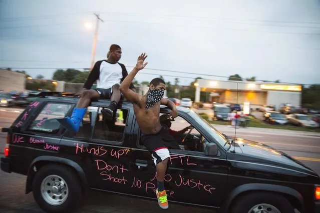 Protesters hang out of a car as they honk their horn and chant during ongoing demonstrations in reaction to the shooting of Michael Brown in Ferguson, Missouri August 16, 2014. Missouri Governor Jay Nixon declared a state of emergency and imposed a curfew in Ferguson on Saturday following a week-long series of racially charged protests and looting over the shooting of the unarmed black teenager by a white police officer. (Photo by Lucas Jackson/Reuters)