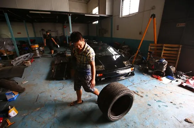 A worker rolls a tyre in front of a handmade replica of Lamborghini Diablo as he works at a garage rented by Wang Yu and Li Lintao on the outskirts of Beijing, August 21, 2014. (Photo by Petar Kujundzic/Reuters)