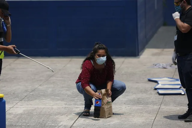 A deported woman looks at her family as she picks up the food they brought her, at the site where Guatemalans returned from the U.S. are being held in Guatemala City, Friday, April 17, 2020. The recently deported Guatemalans were placed in a athletic dorm facility to wait for the results of their tests for the new coronavirus. (Photo by Moises Castillo/AP Photo)