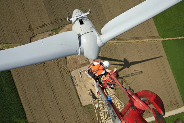 Employees work on a crane above an E-70 wind turbine manufactured by German company Enercon for La Compagnie du Vent during its installation at a wind farm in Meneslies, Picardie region, France July 31, 2014. (Photo by Benoit Tessier/Reuters)