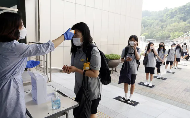 Students wearing face masks to help protect against the spread of the new coronavirus stand in a line to have their body temperatures checked before entering their classrooms at a middle school in Chungju, South Korea, Monday, June 8, 2020. (Photo by In Jin-hyun/Newsis via AP Photo)