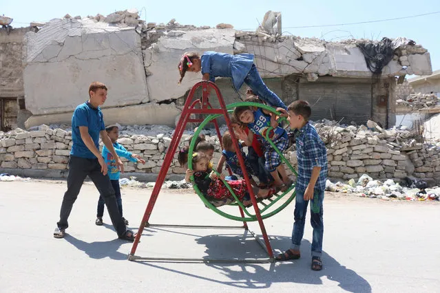 Syrian children play on a swing in front of a damaged building in rebel-held side of Aleppo on July 6, 2016, during celebrations for Eid al-Fitr, which marks the end of the Muslim holy fasting month of Ramadan. (Photo by Thaer Mohammed/AFP Photo)