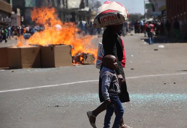 A woman and child pass a fire set alight during a protest in Harare, Friday, August 26, 2016. The demonstration organised by opposition political parties calling for reforms, is the first time that the fractured opposition has joined forces in a single unified action to confront President Robert Mugabe's government. (Photo by AP Photo)