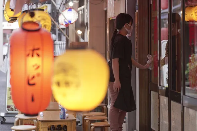 An employee wearing a mask against the spread of the new coronavirus cleans windows of a Japanese pub in Tokyo Monday, July 20, 2020. The Japanese capital confirmed Monday more than 160 new coronavirus cases. (Photo by Eugene Hoshiko/AP Photo)