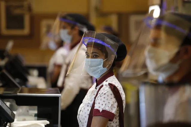 Workers of PVR cinemas, a multiplex cinema chain, stand at the food court with face shields and masks during a press preview to show their preparedness with the COVID-19 pandemic in New Delhi, India, Friday, July 31, 2020. (Photo by Manish Swarup/AP Photo)