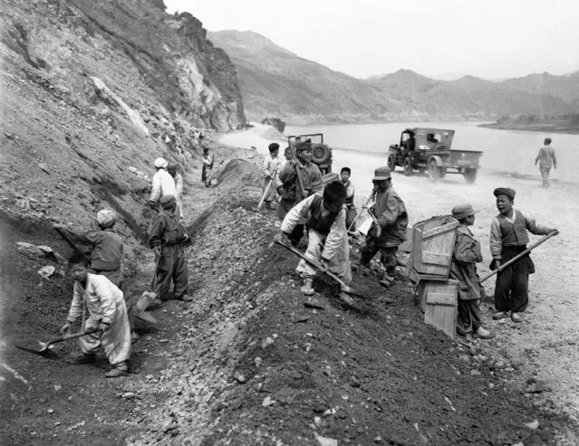 Wearing ill-fitting clothes, some of GI origin, these young Koreans aid in road repair on April 25, 1942. Youngster at right appears to be having difficulty with a co-worker who holds box-like contraption on his back. This box is filled with dirt and operates by opening hinged boom with rope carried over the shoulders. When dirt has been carried to desired location, the hinged bottom is lowered and the dirt settles where needed. (Photo by Gene Smith/AP Photo)