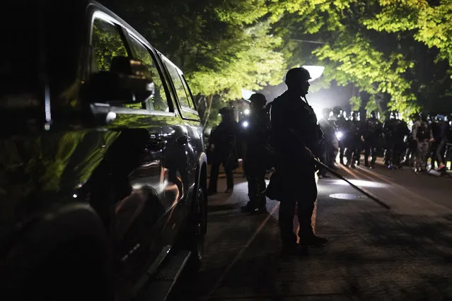 Portland police officers walk through the Laurelhurst neighborhood after dispersing protesters from the Multnomah County Sheriff's Office early in the morning on Saturday, August 8, 2020 in Portland, Ore. (Photo by Nathan Howard/AP Photo)