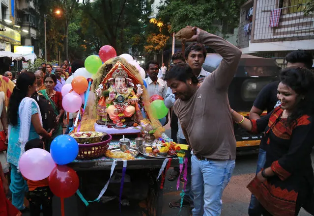 In this Tuesday, September 6, 2016 photo, a relative of Raju Laljibhai Dipikar performs the ritual of breaking a coconut in front of an idol of elephant-headed Hindu god Ganesha as they prepare to set out for its immersion, on the second day of Ganesha Chaturthi festival in Mumbai, India. Every year Dipikar goes out with his family to choose an elaborate statue of the Ganesha and for two days the god “lives” with the family in their tiny apartment in Mumbai, his very presence bringing them joy. And in return for the love the family showers on him he takes away all their problems, Dipikar says. While families immerse the idols installed in their homes at different points in the ten-day celebration, it's the tenth day that makes for the most grand spectacle. (Photo by Rafiq Maqbool/AP Photo)