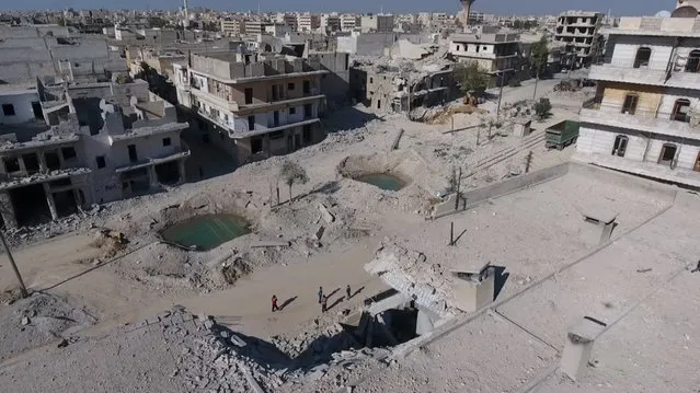 A still image taken on September 27, 2016 from a drone footage obtained by Reuters shows people standing near craters and damaged buildings in a rebel-held area of Aleppo, Syria. (Photo by Reuters TV)