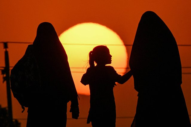 Two women and a girl march with other Shiite Muslim devotee in the Midaina district in the north of Iraq's Basra province at sunset on July 30, 2025 as they make their way to the shrine city of Karbala joining the Arbaeen pilgrimage, marking 40 days after commemorations of the seventh century killing of Prophet Mohammed's grandson Imam Hussein. (Photo by Hussein Faleh/AFP Photo)