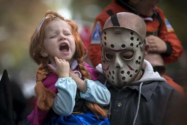 A child struggles to keep hair out of her mouth as she is carried by an adult in a mask as they take part in the Children's Halloween day parade at Washington Square Park in the Manhattan borough of New York October 31, 2015. (Photo by Carlo Allegri/Reuters)