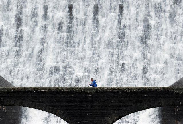 A man walks in front of water cascades over the Caban Coch dam in the Elan Valley, Wales, Britain on November 16, 2020. (Photo by Carl Recine/Reuters)